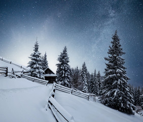 Wall Mural - Winter landscape. Mountain village in the Ukrainian Carpathians. Vibrant night sky with stars and nebula and galaxy. Deep sky astrophoto