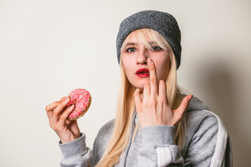 Beautiful girl eating pink donut showing fuck. Beauty fashion youth, enjoying the food, eat colorful donut. Diet diet concept. Junk food, weight loss.