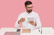 © WHstudio Leushin N - Pensive bearded young man wears spectacles, browses web page, holds touch pad, drinks disposable cup of coffee, connected to wireless internet, focused aside, wears formal clothes at workplace.