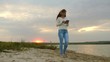 girl with headphones walking along beach with tablet and listening to music. girl in rays of sunset walking on beach and checking mail on tablet online