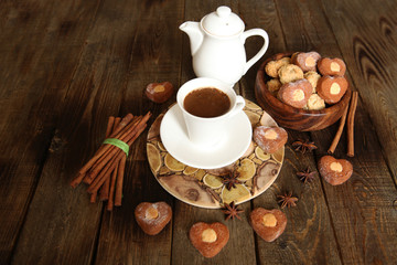 cup of coffee with a saucer and a white kettle with heart-shaped cookies on a rustic wooden table