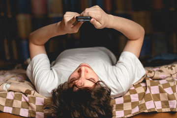 young male lay on bed upside down and chat in his mobile phone gadget f