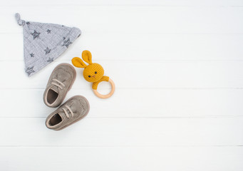 Wall Mural - Newborn baby hat, shoes and rabbit beanbag on white wooden background