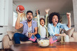 © Mediteraneo - Happy African American family of three watching tv and cheering sport games on sofa at home
