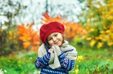 Portrait of a little girl in the fall in nature . Baby in a red beret and a warm sweater