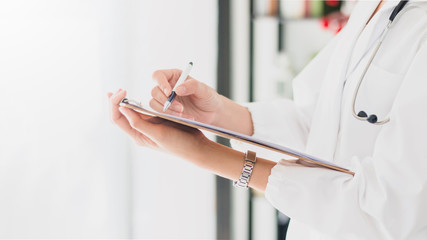 Wall Mural - The female doctor is holding and writing medical report on hand to treat the patient in hospital.The concept of good health care by regularly checking health.