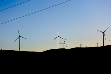 Wall Mural - Silhouette view of a wind turbines on top of mountains, sunset sky