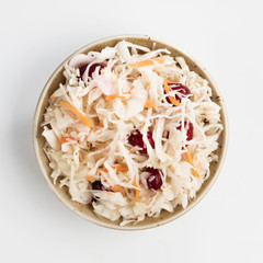 Traditional russian appetizer sauerkraut with cranberry and carrot in craft plate isolated on white. Fermented cabbage. Russian cuisine and russian kitchen. Top view or flat-lay.