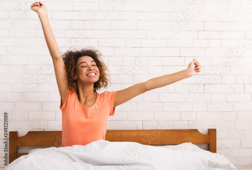 Fotografía African-american woman stretching, sitting on bed in morning