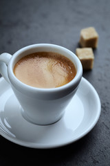 Cup of coffee and two brown sugar cubes on black stone background. Close up. 