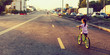© Angelov - Little brunette girl riding bicycle on road at sunset