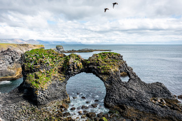 Landscape view of famous Gatklettur arch rock near Hellnar National park Snaefellsnes Peninsula in Iceland with two birds flying on summer day