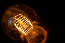 Top Of View Of Turn On In Slow Motion With Dust, Retro Vintage Light Bulb With Old Technology With Filament Built-in With Warm Light Yellow Tint And Black Background, Vintage Object Old