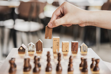 Hand choosing mini wood house model from chess game, Choose what's the best. A symbol for construction ,ecology, loan, business financial district and commercial ,success and leadership concepts.