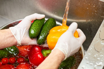 Yellow bell bepper and cucumbers washing by tap water. Vegetables in a kitchen sink.