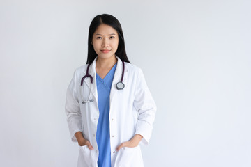 Content young female doctor posing at camera. Pretty woman wearing white coat and standing. Medicine and healthcare concept. Isolated front view on white background.