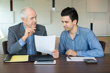 Wall Mural - Business partners discussing contract. Serious senior entrepreneur explaining work to his young coworker. Business meeting concept