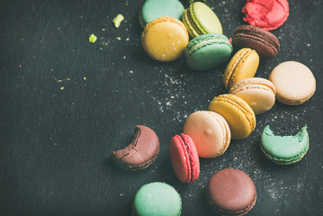 Sweet colorful French macaroon cookies variety with sugar powder over black background, top view, selective focus, copy space