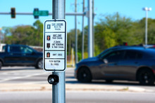 Traffic Intersection Pedestrian Crosswalk Crossing Sign With Signal Descriptions Above The Request Button With Cars And Lights In The Background.