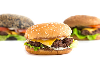 Big burger close up on a white background. Beef patty burger, cheddar cheese, lettuce, bacon, pickled cucumber, tomato and balsamic sauce. In the background are two burgers.