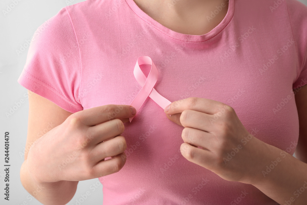Woman with pink ribbon on light background, closeup. Breast cancer awareness concept