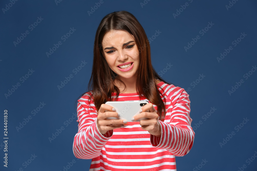 Emotional young woman playing mobile game on color background