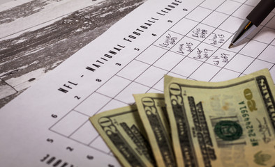 Football office pool grid for sports betting concept with money and a pen, partially completed boxes