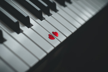 Two small red hearts on the keyboard of classic piano close up. Concept of love and romantic music