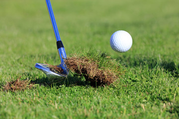 chipping golf ball out of the rough grass with a big divot