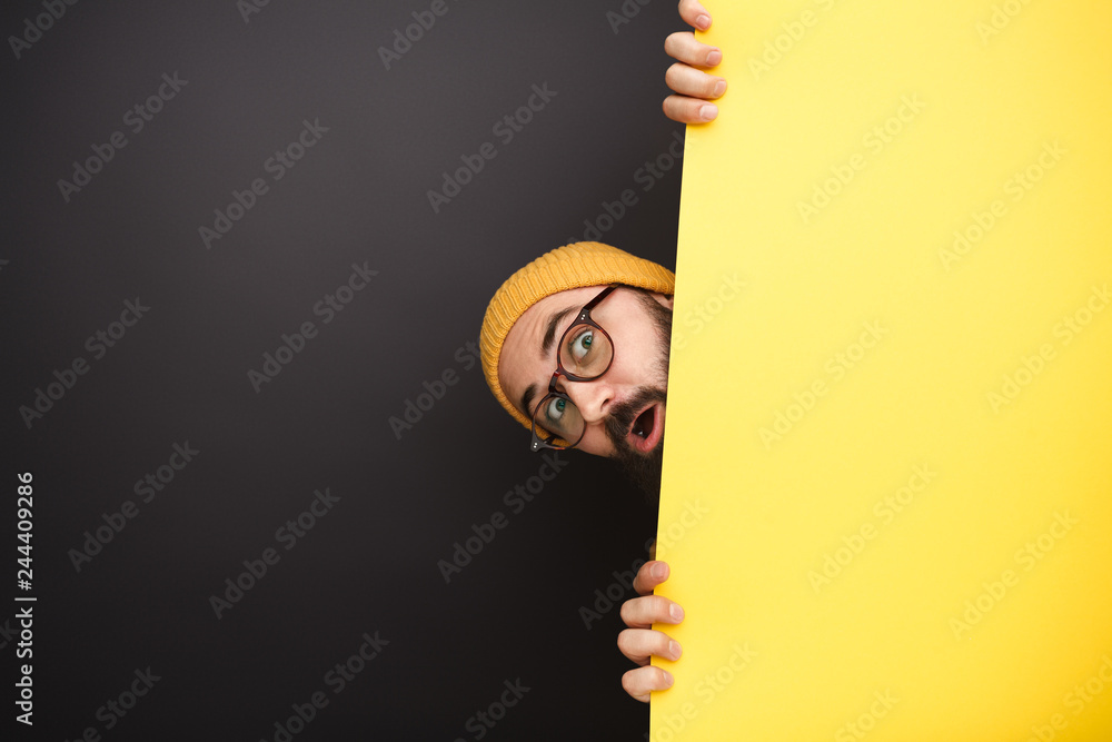 Funny man peeking out from behind yellow banner - obrazy, fototapety, plakaty 