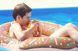 © Natali - Cute sporty boy swims in the pool with donut ring and has fun, eats oranges. Vacation with kids, holidays, active weekends, summer concept. Chocolate donut