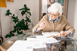 © Seventyfour - Warm toned portrait of senior woman filling tax forms at home, copy space
