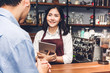 © Art_Photo - Portrait of woman small business owner working behind the counter bar in a cafe.Barista using tablet and receive order from customer