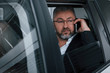 © standret - Boss is on the work. Having business call while sitting at the back of modern luxury car. Senior man in glasses and official wear