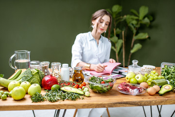 Wall Mural - Woman dietitian in medical uniform working on a diet plan sitting with different healthy food ingredients in the green office