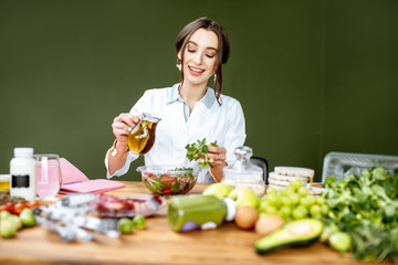 Wall Mural - Woman dietitian working on a healthy diet pouring olive oil into the salad sitting at the table full of various healthy food indoors