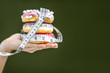 Three sweet donuts covered with measurement tape on the hand on the green background. Unhealthy eating and adiposity concept