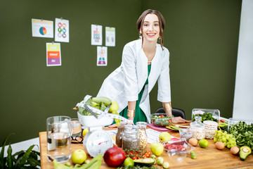 Wall Mural - Portrait of a young woman nutritionist standing near the table full of healthy products in the green office