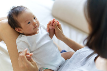 asian newborn baby sitting on mother knees. she is looking at her mom and smile. mother holding baby