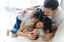 Happy Family At Home. Asian Father, Mother And Sister On Sofa Are Smiling, Laughing And Playing With Newborn Baby, New Member Of Their Family. They Spent A Great Time Together. Happy Family Concept.