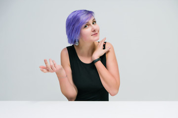 Talk to me - Concept portrait of a beautiful girl with purple hair on a white background sitting at the table and talking.