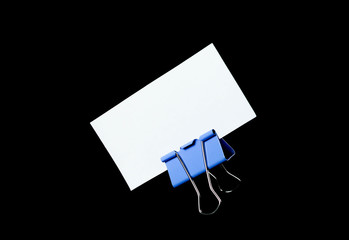 An empty white business card stands on a stationery clip. Close up. Isolated on black background