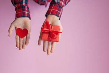 Child hands holding red paper heart and box present in hands on pink background. Valentines day concept.