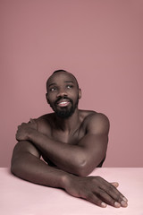 Wall Mural - Portrait of a young naked happy african man at studio. High Fashion male model posing on pink background