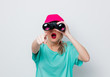 Beautiful young girl in pink cap and blue t-shirt looking for something with binocular on white background.