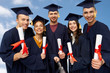 © Syda Productions - education, graduation and people concept - group of happy graduate students in mortar boards and bachelor gowns with diplomas taking picture by slfie stick over blue sky and clouds background