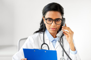 Wall Mural - medicine, people and healthcare concept - indian female doctor with clipboard calling on phone at hospital