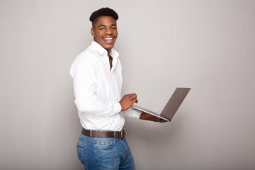 Side of happy young black man holding cellphone by gray wall