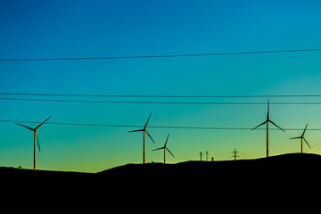 Wall Mural - Silhouette view of a wind turbines on top of mountains, sunset sky