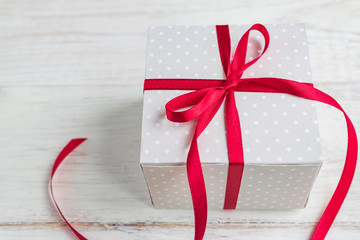 Beige polka dot gift box with red ribbon bow on wooden background.